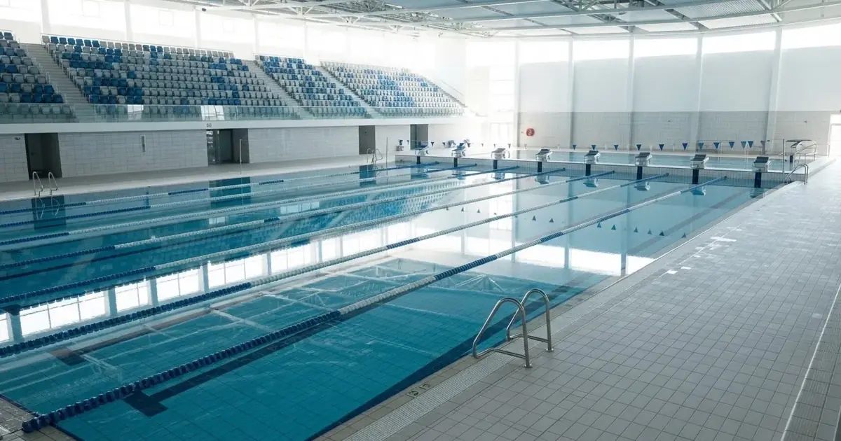 Pusty basen olimpijski z równymi torami i spokojną taflą wody, widok z trybun w jasnym świetle.